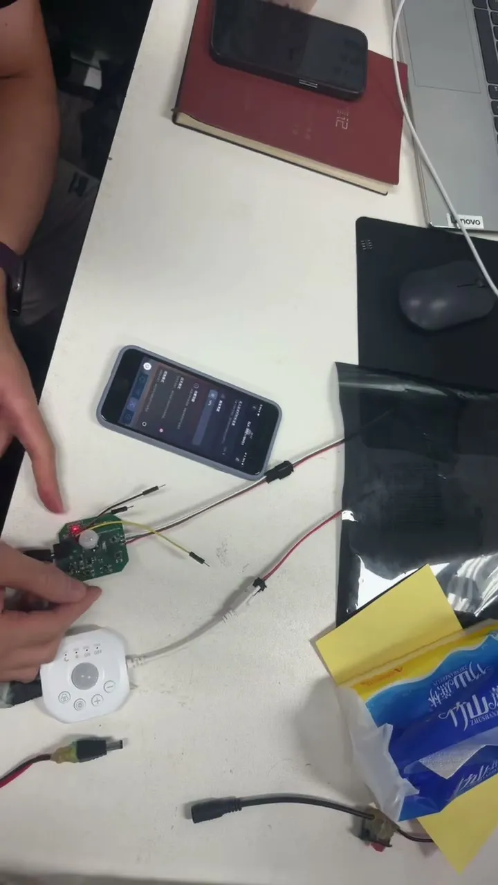 A phone running the control app on a desk beside a controller board and a lit LED strip.