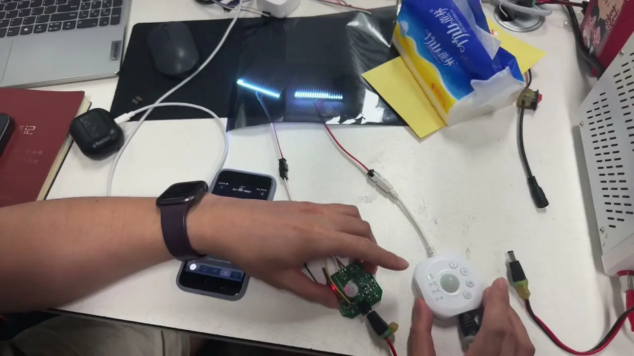 A desk with a controller, a phone and an LED strip lit blue, wired to a bench supply.