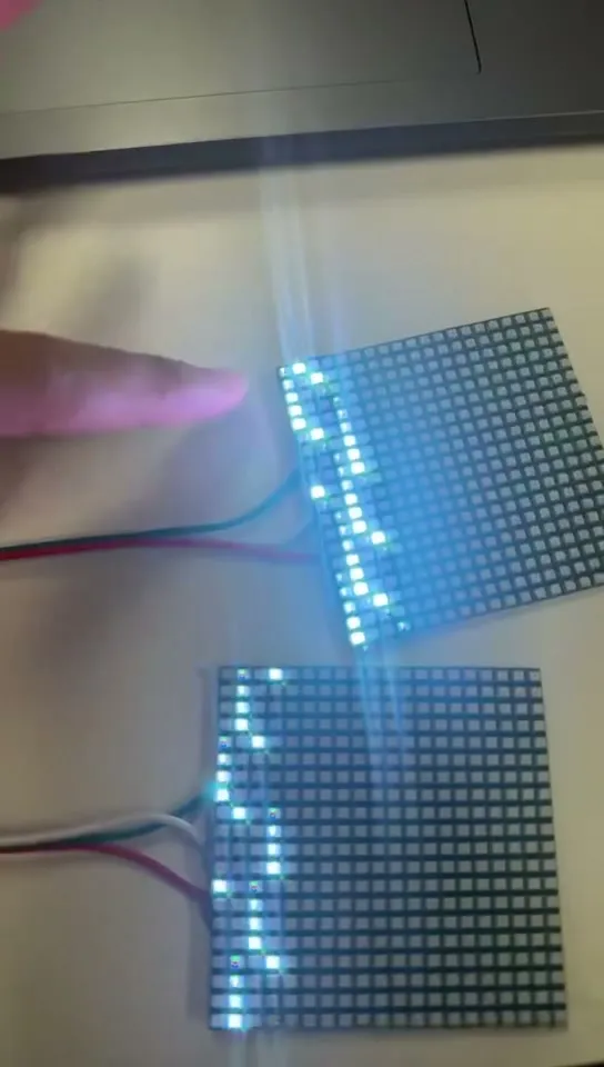 Two LED matrix panels on a bench, lit white and blue, wired to a controller.