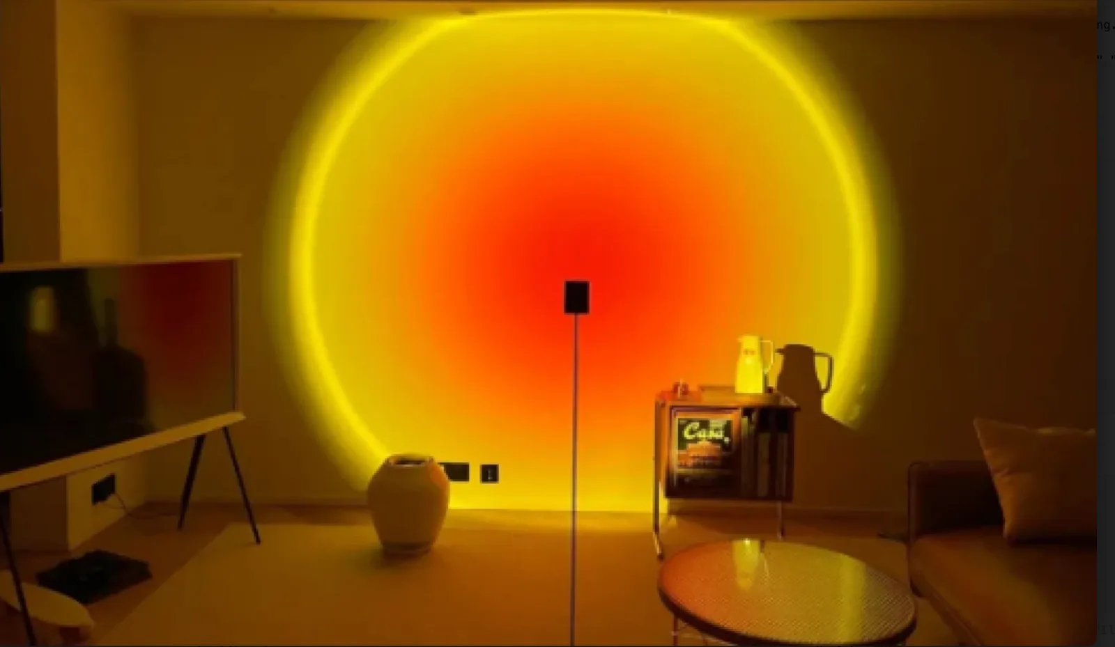 A sunset lamp on a floor stand projecting a large orange and yellow disc onto a plain living room wall at night.